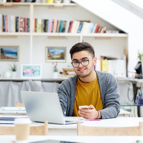 Handsome student sitting by desk in classroom